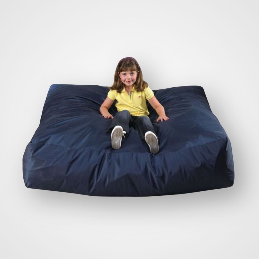 A child sitting on a large navy blue therapy impact cushion designed for sensory play and regulation. Child jumping onto a large impact cushion β therapy tool for energy release, body awareness, and self-regulation through movement.