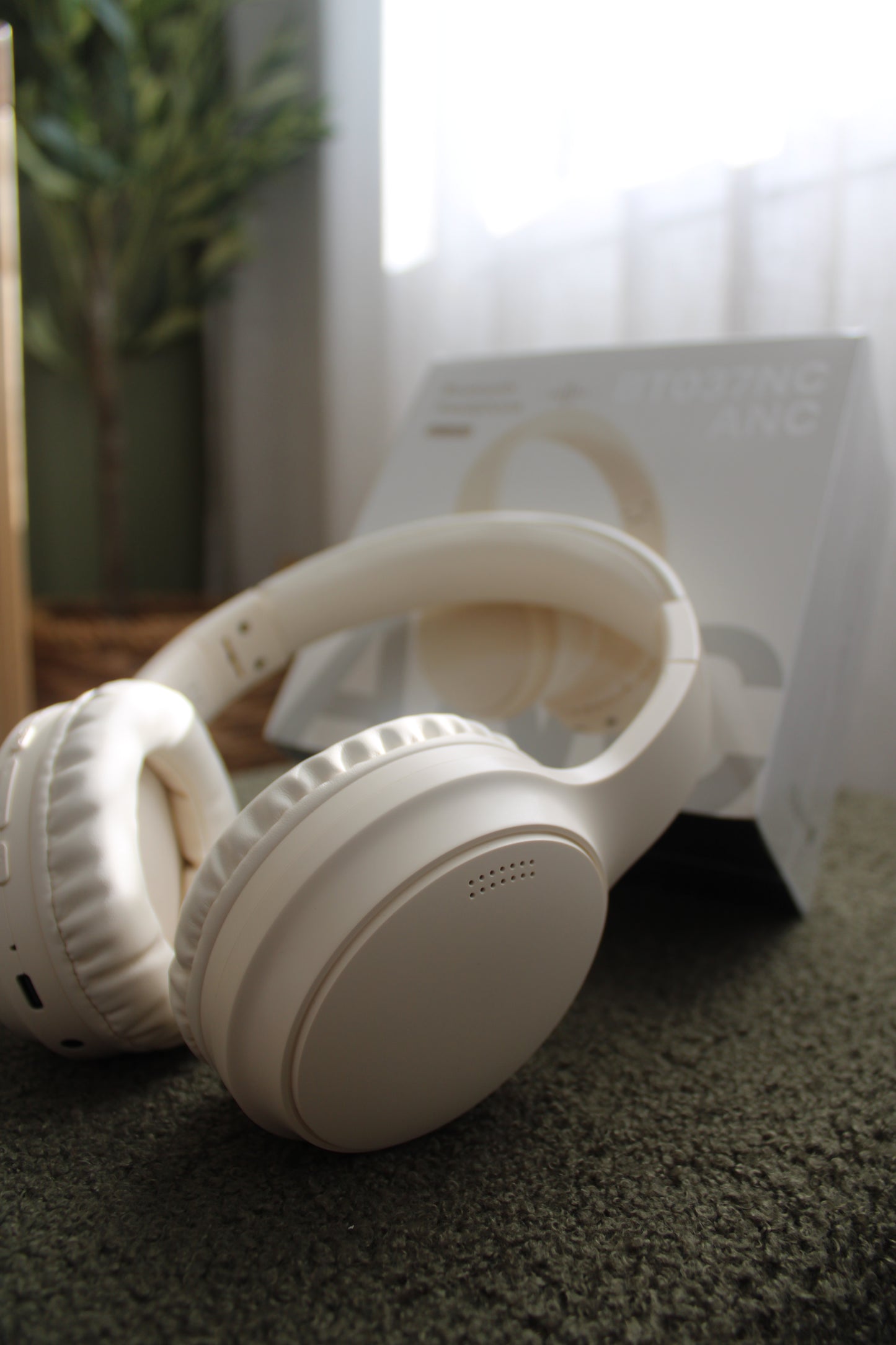 A pair of white noise-cancelling Bluetooth headphones placed on a surface with a product box in the background. Wireless noise reducing headphones placed in classroom or therapy setting – helping create a calm and focused environment.