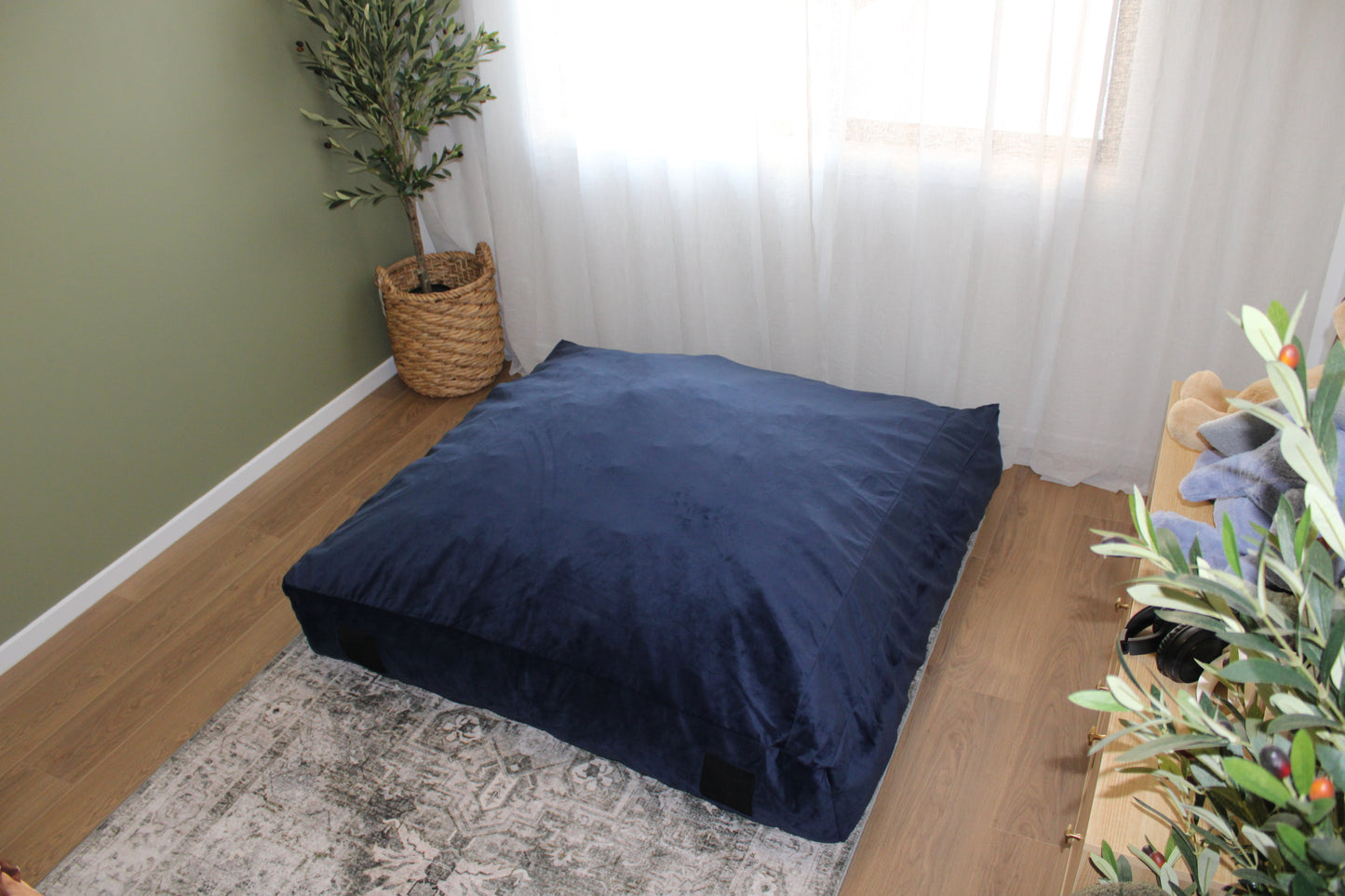 A large navy blue therapy impact cushion placed on the floor in a room with a window and a potted plant. Therapy impact cushion placed in playroom or clinic – supportive crash pad for behavioural regulation and physical exploration.