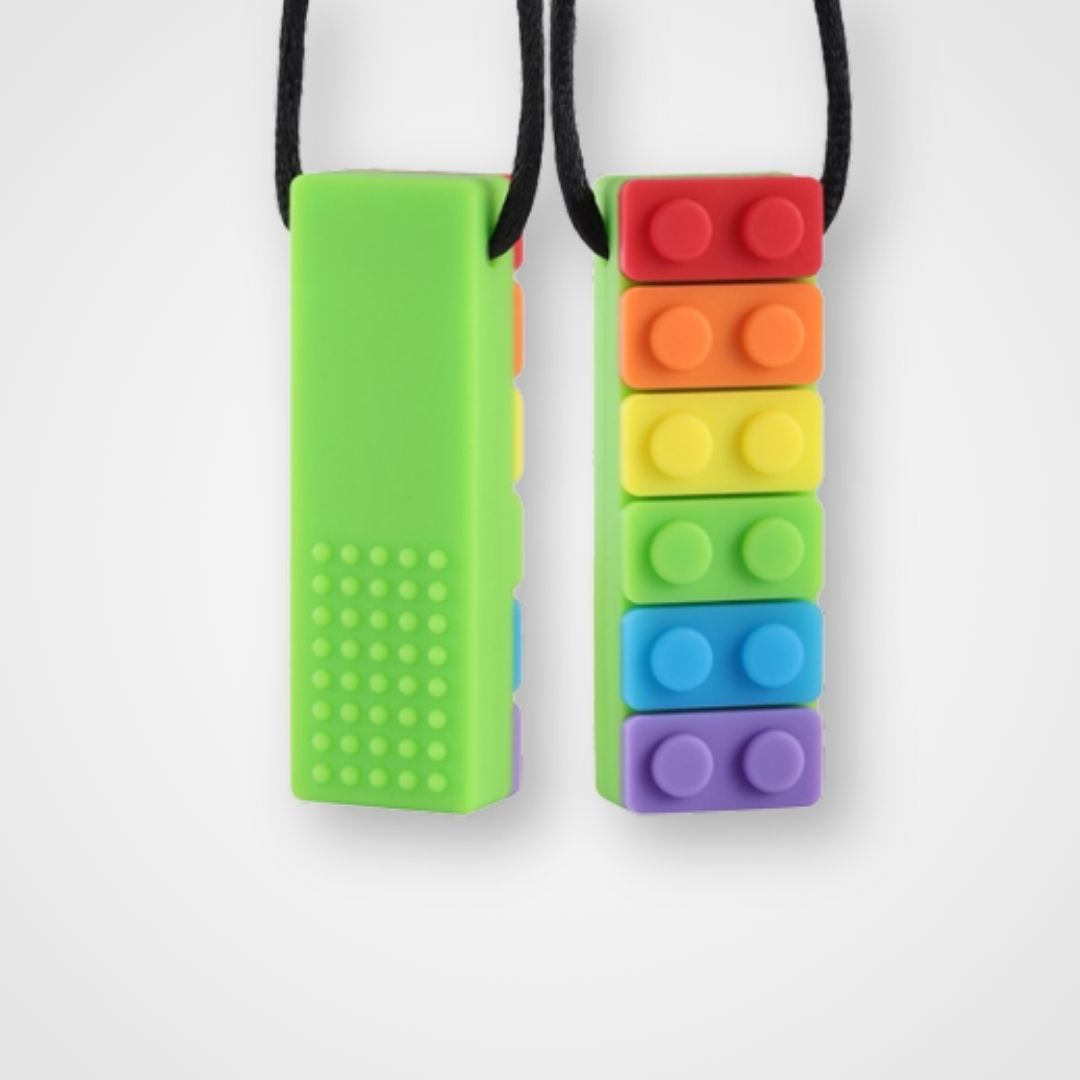 A chewable silicone necklace with a discreet green body and colorful, block-shaped elements on one side, attached to a black strap. Chew-safe oral therapy necklace made from food-grade silicone – designed to support focus, calm, and self-regulation.